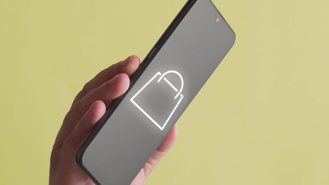 persona que sostiene un teléfono móvil donde aparece la animación de un símbolo de compras en línea, fondo amarillo