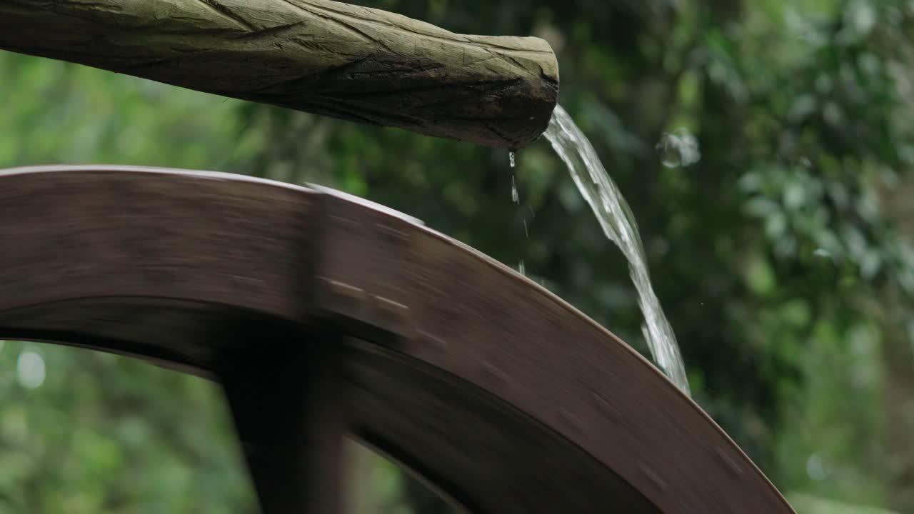 Detailed close up shot of fresh water pouring from a wooden spout directly onto the blades of a traditional rustic water wheel