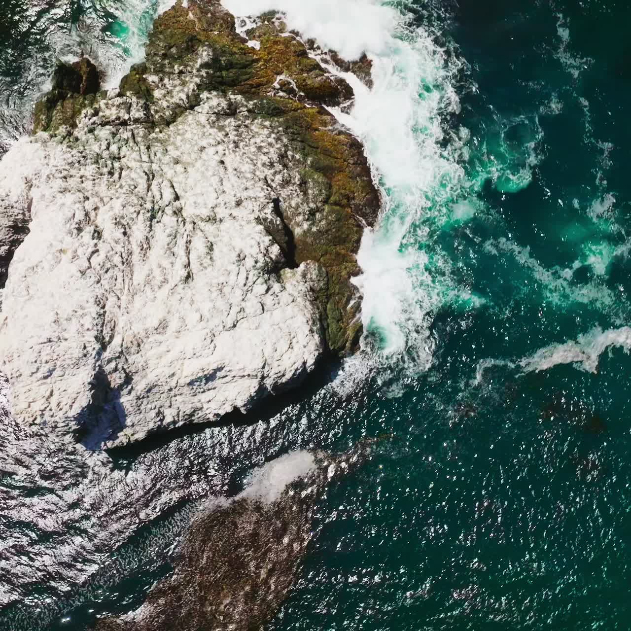 Big stone peeping from the blue water. White foamy waves crushing by the rock on sunny daytime. Bird's eye view