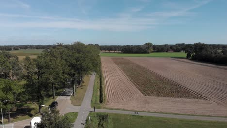 Aerial-following-of-a-clean-asphalt-country-road-and-bike-lane-in-The-Netherlands-with-trees-on-either-side-against-a-blue-sky