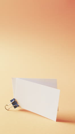 vertical video of blank white business cards with bulldog clip on orange background, copy space