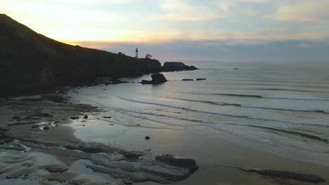 aerial shot pushing towards a lighthouse in newport, oregon looking out over the sunset