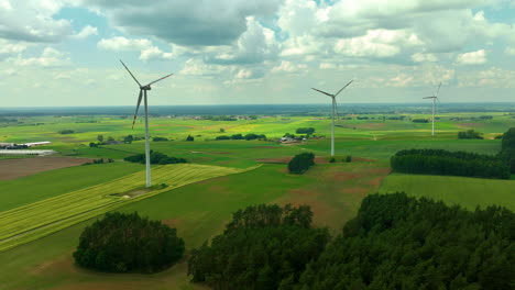 Luftaufnahmen-Zeigen-Windturbinen,-Die-Hoch-über-Einer-Weitläufigen-Ländlichen-Landschaft-Mit-Grünen-Feldern-Und-Baumgruppen-Stehen