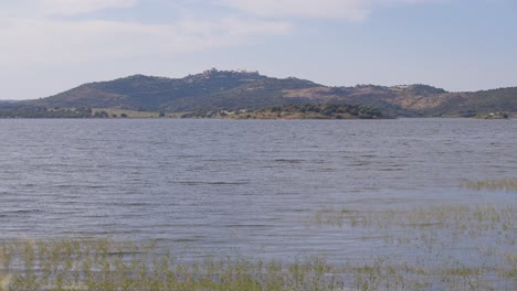 Una-Encantadora-Vista-A-Nivel-Del-Suelo-De-Monsaraz-Desde-Los-Prados-Llenos-De-Hierbas,-Que-Captura-La-Exuberante-Vegetación-Y-El-Encanto-Atemporal-Del-Pueblo-Medieval-En-Contraste-Con-El-Pintoresco-Paisaje