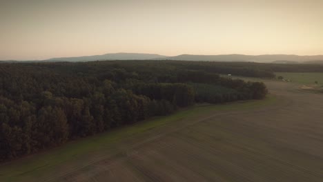 Dramatische-Und-Epische-Drohnenaufnahme-Der-Wälder-Und-Felder-Mit-Bergen-Im-Hintergrund,-Vogelperspektive,-Während-Eines-Sonnenuntergangs-Oder-Eines-Sonnenaufgangs,-Der-Dämmerung-Oder-Der-Morgendämmerung