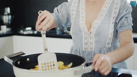 Side-view:-Attractive-young-woman-fries-potatoes-on-a-modern-electric-stove-with-a-built-in-extractor-fan