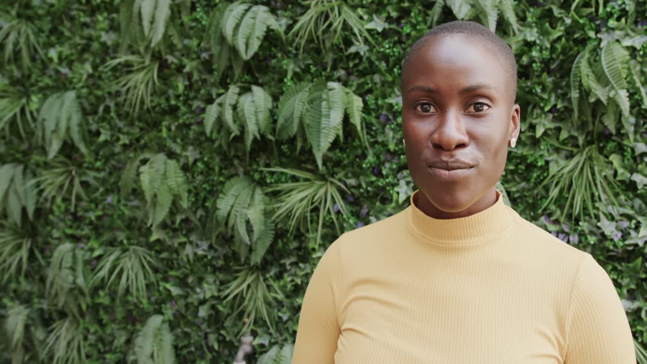 retrato de una feliz mujer afroamericana sonriendo frente a una pared de plantas, espacio de copia, cámara lenta