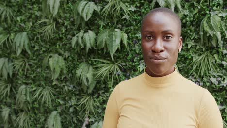 portrait of happy african american woman smiling in front of wall of plants, copy space, slow motion
