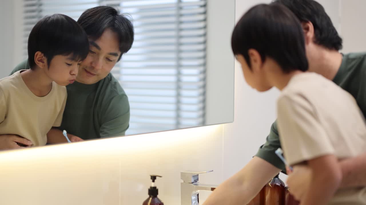 Father helps young son brush teeth in bright bathroom, highlighting caring family morning routine