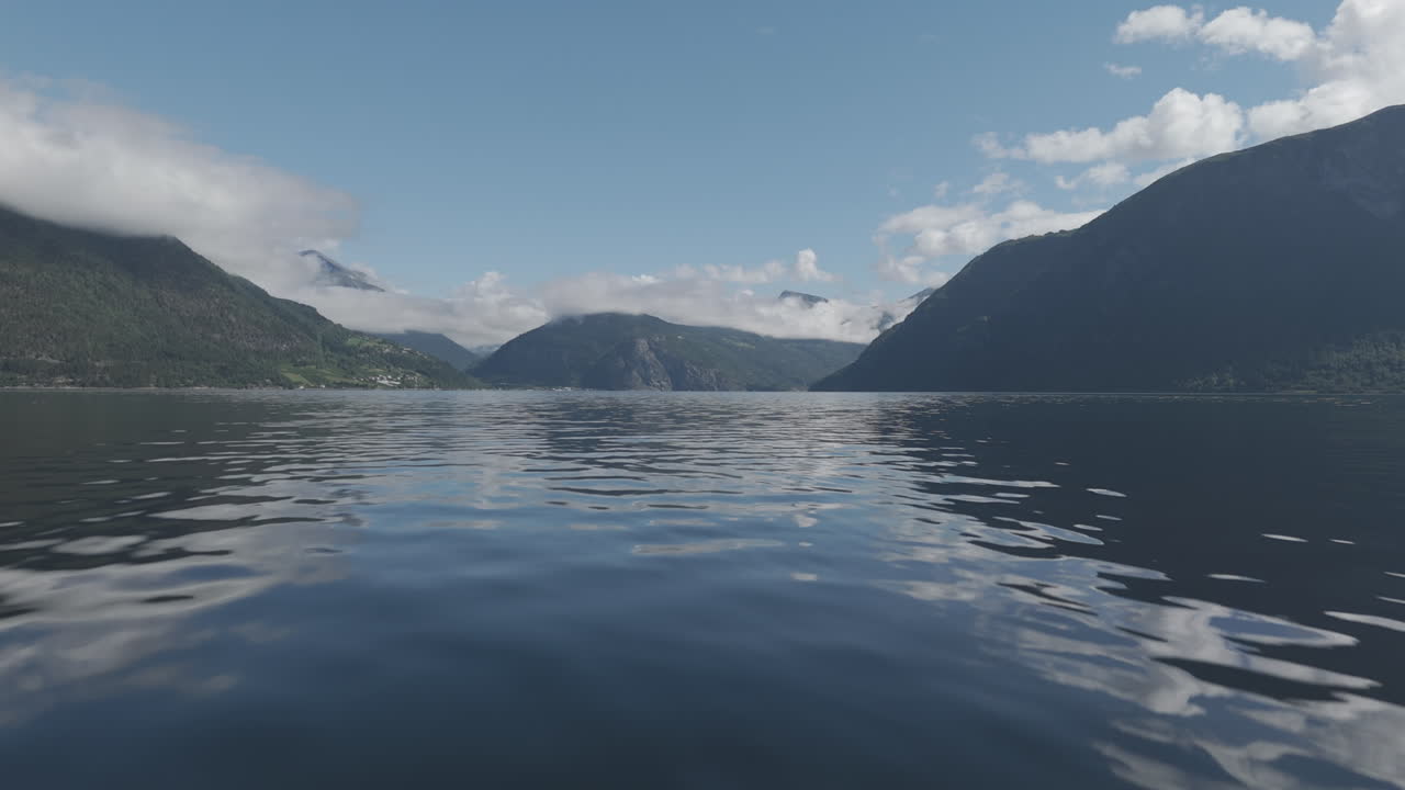 노르웨이의 피오르드를 향해 물에 가까이 다가오는 느린 속도 드론 은 고 구름이 많은 날, 배경에는 산과 초록색과 반사되는 물 로그가 있습니다.