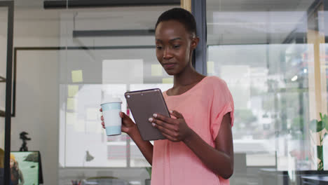 Mujer-De-Negocios-Afroamericana-Bebiendo-Café-Para-Llevar-Usando-Una-Tableta-Y-Sonriendo-A-La-Cámara-En-La-Oficina