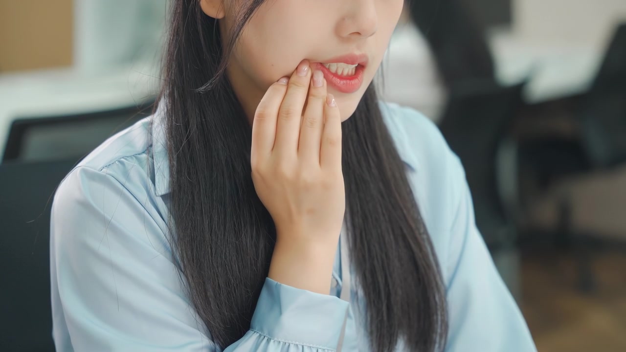 デスクワーク中の女性オフィスワーカーが口の痛みを訴えている。唇の乾燥、口内炎、虫歯、歯痛、アフタ性口内炎、口腔病変、歯肉炎、歯周病に悩まされている。