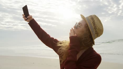 Side-view-of-young-beautiful-caucasian-woman-clicking-selfie-with-mobile-phone-at-beach-4k