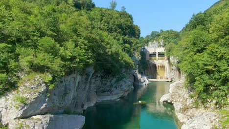 Drone-flying-low,-over-a-narrow-fresh-water-stream-amidst-green-hills-with-hidden-caves-and-waterfalls