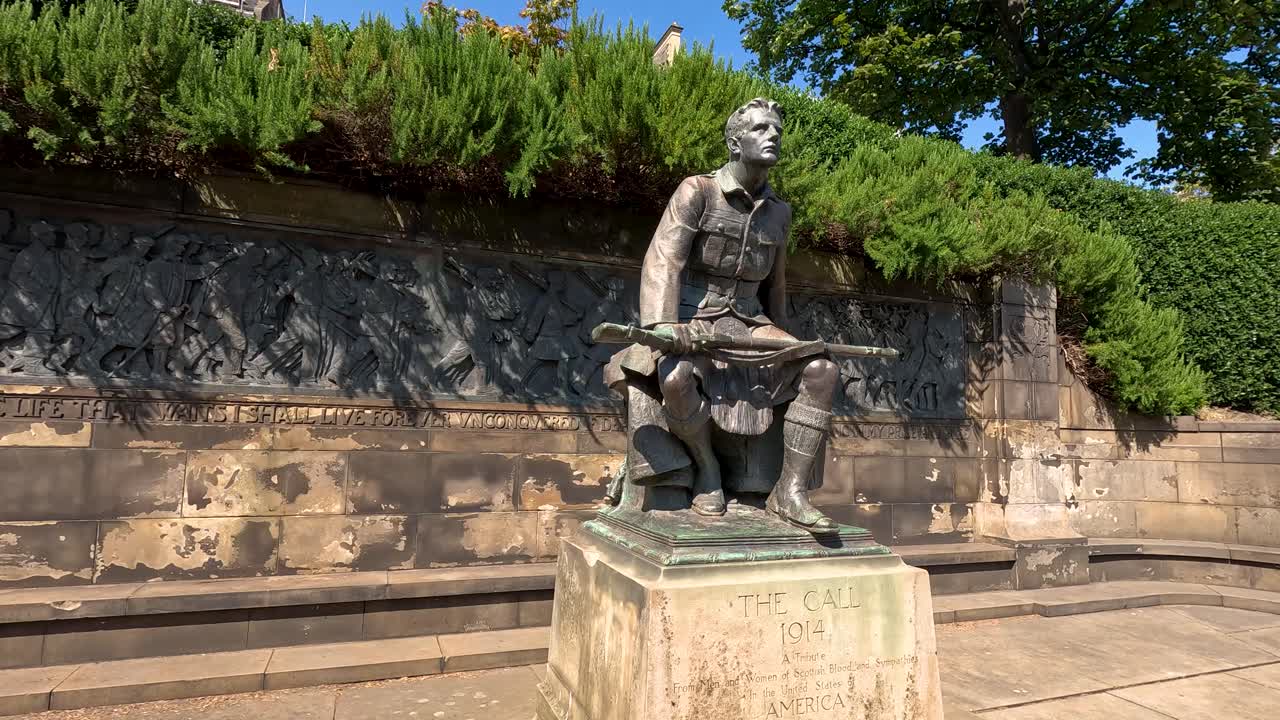 Daytime video pans around a bronze World War I soldier statue, The Call, in a sunlit outdoor plaza with stone walls and greenery in Edinburgh
