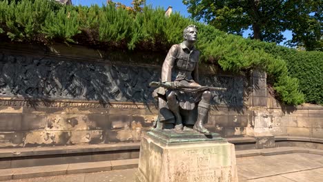 daytime video pans around a bronze world war i soldier statue, the call, in a sunlit outdoor plaza with stone walls and greenery in edinburgh
