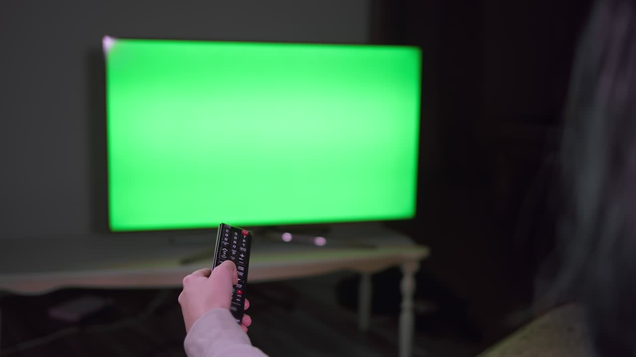 손에 리모컨을 들고 채널을 바꾸는 소녀, 밤에는 tv 근처에 앉아, 녹색 화면