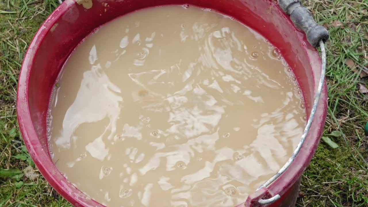 The girl washes her hands in a bucket of clay water dirty. Outside. Hendheld.