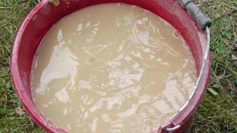 the girl washes her hands in a bucket of clay water dirty. outside. hendheld.