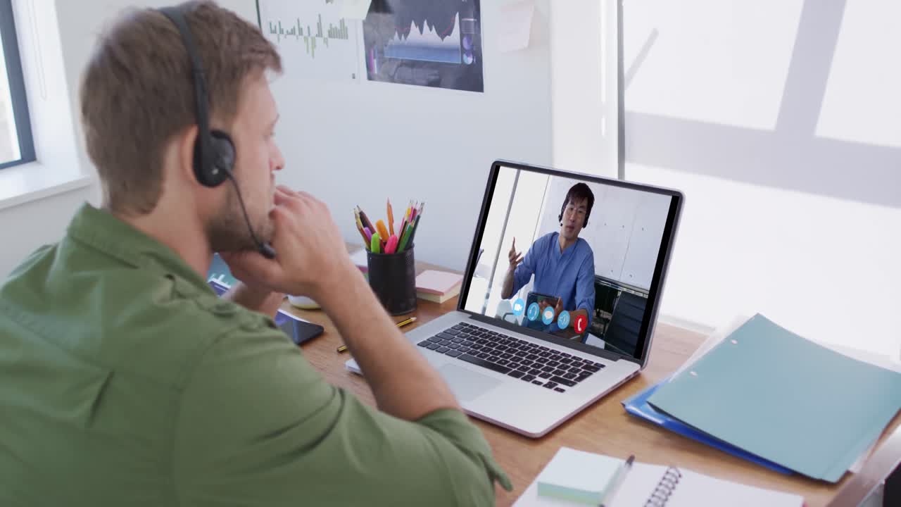 Kaukasisk mand bruger bærbar computer og telefonheadset på videoopkald med en mandlig kollega.