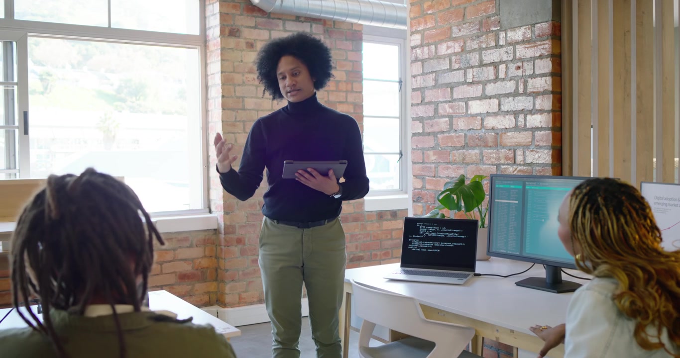 African American man tapping tablet leading meeting in office reviewing laptop code monitor charts