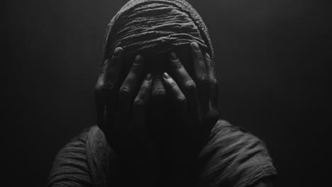 a mummified woman against the dark background in keeps her hands on her face the powerful pose full of despair