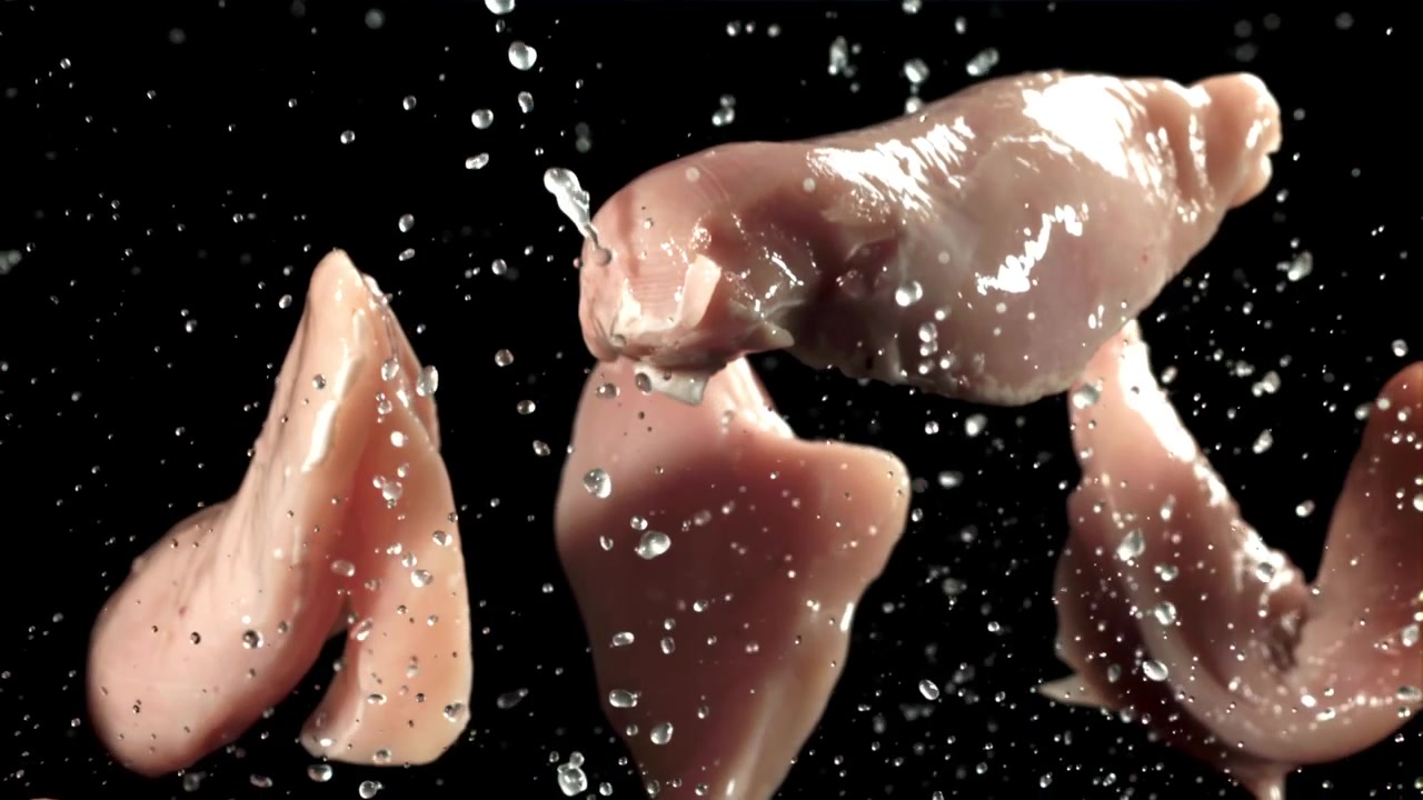 Filetti di pollo crudi schizzati d'acqua su sfondo nero