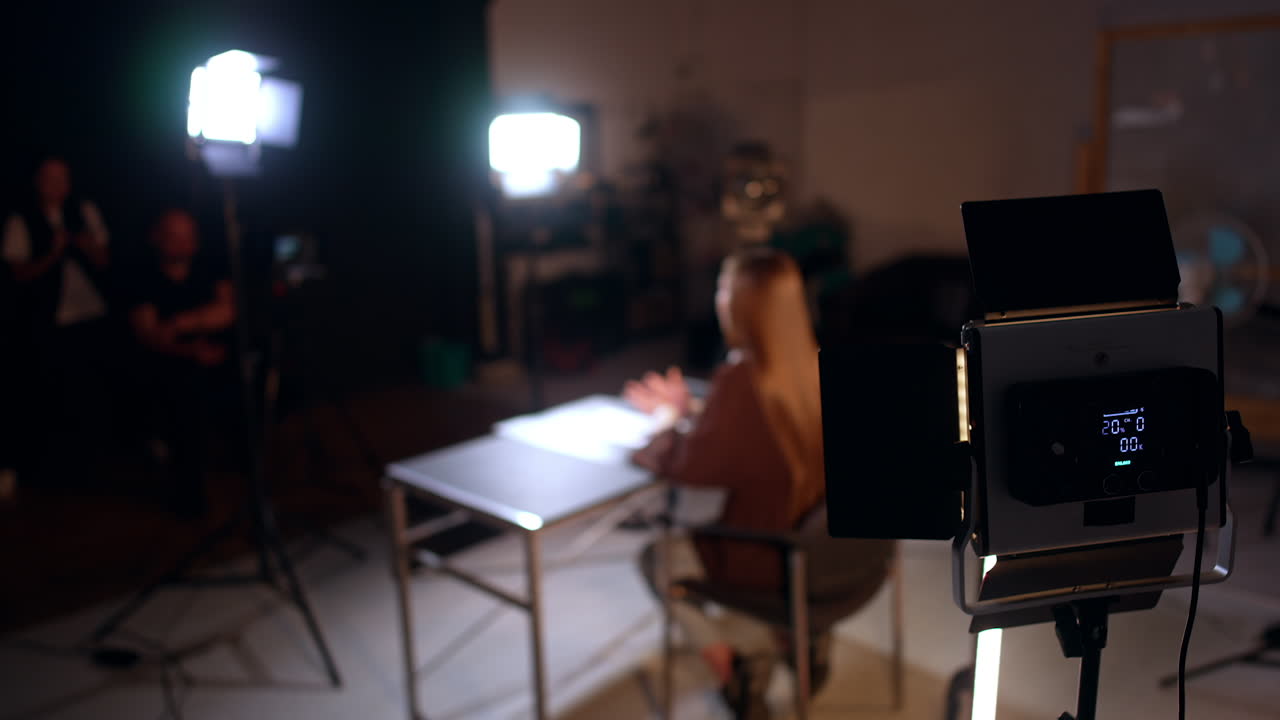 Soffits illuminate a woman sitting in studio at desk. Behind the stages in the modern photo studio during footage.
