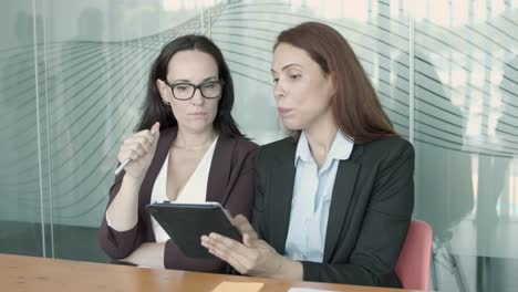 two pretty businesswomen sitting together and watching at tablet