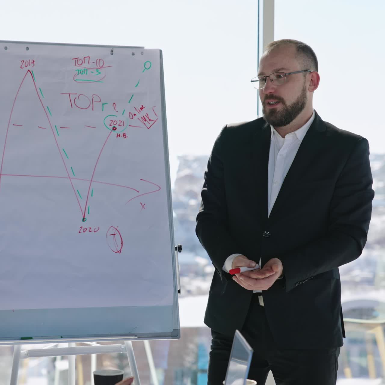 Emotional speech in front of the colleagues at the meeting. Businessman standing in front of the flip chart presents the infographics. Cityscape blurred at the backdrop