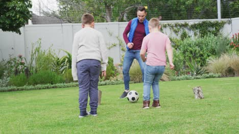 happy caucasian father with two sons playing football in garden
