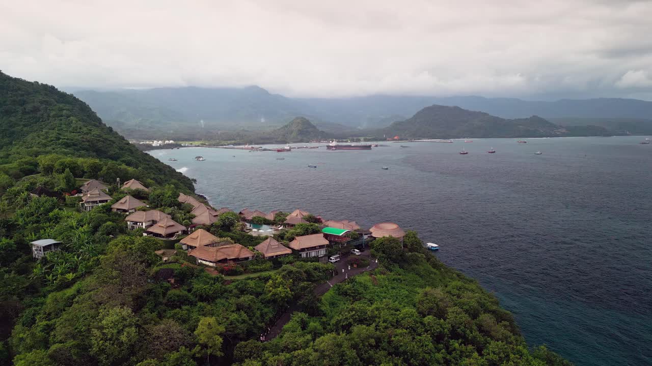 Captivating aerial footage of a hilltop resort above Padang Bai Bali featuring lush tropical scenery, boats on calm water, and panoramic views of the harbor and surrounding landscape
