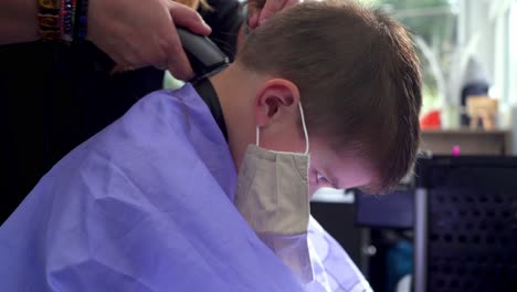 peluquero corta el pelo de un niño caucásico en la peluquería, usando una recortadora