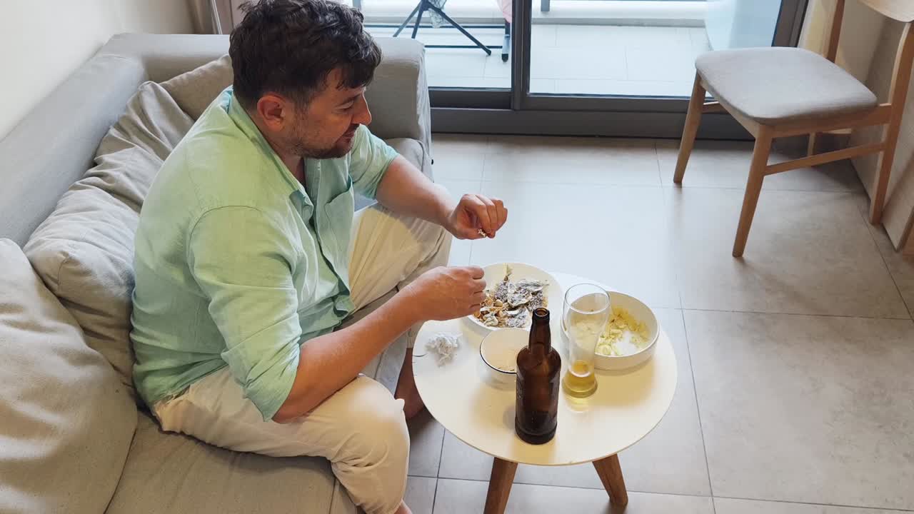 Man relaxing on a couch, eating snacks and drinking beer