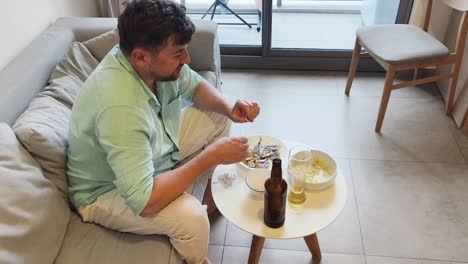 man relaxing on a couch, eating snacks and drinking beer