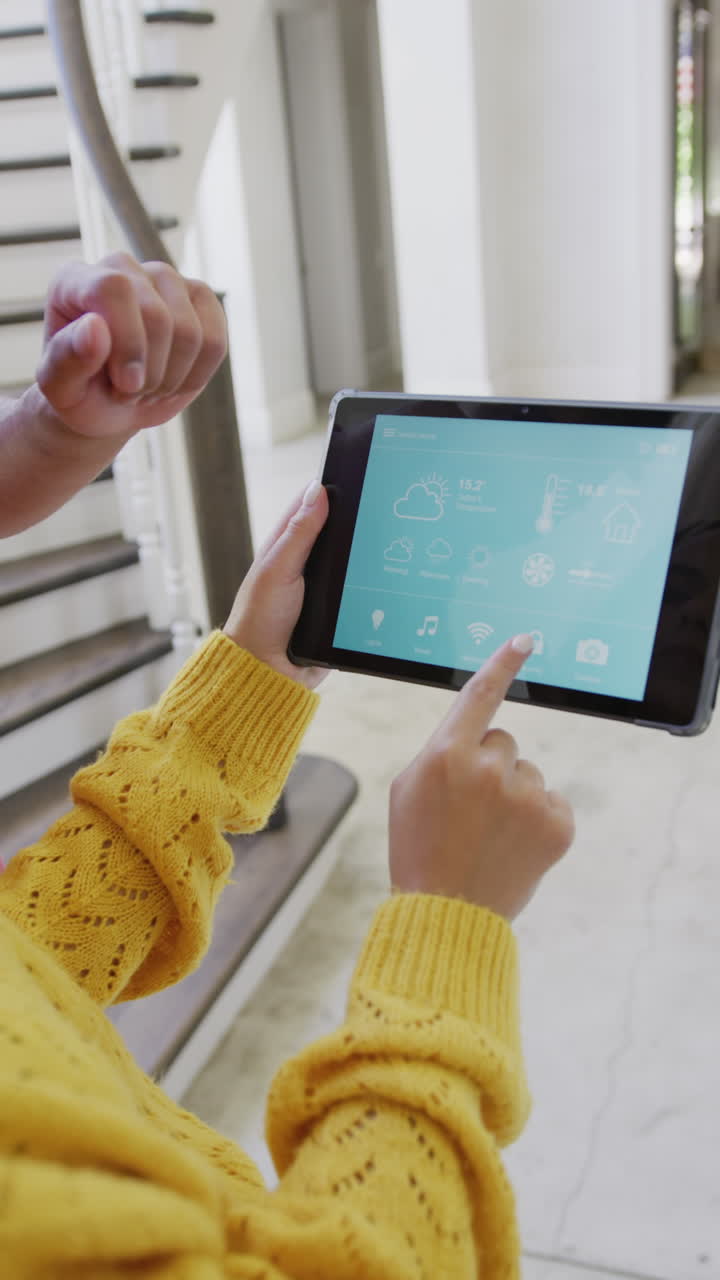 Vertical video of biracial couple spending time at home using tablet with smart home interface