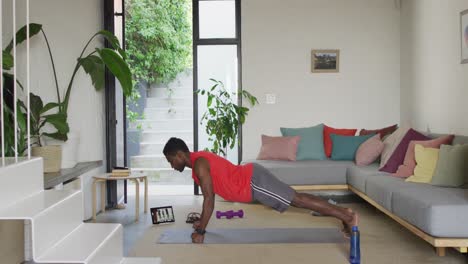 Happy-african-american-man-exercising-in-living-room,-using-tablet