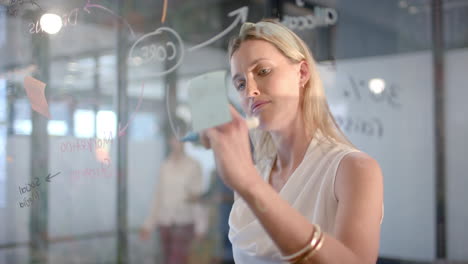 caucasian businesswoman writing on glass wall in office with copy space