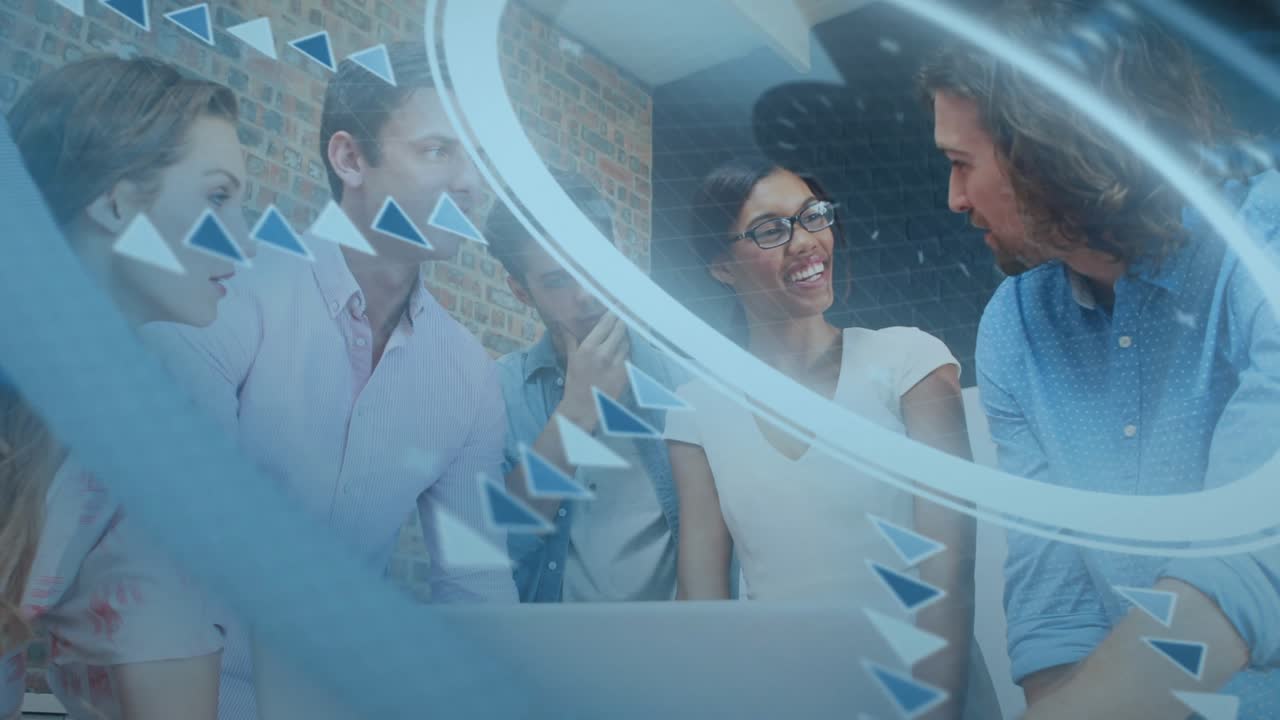 Team gathering around laptop in tech, woman gesturing keyboard driving chat amid rotating graphics