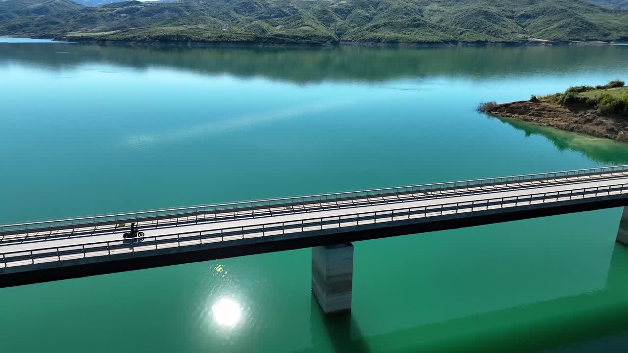 화창한 날 지역 샷 4k 60fps에서 푸른 호수가 내려다보이는 긴 빈 다리를 타고 있는 바이커