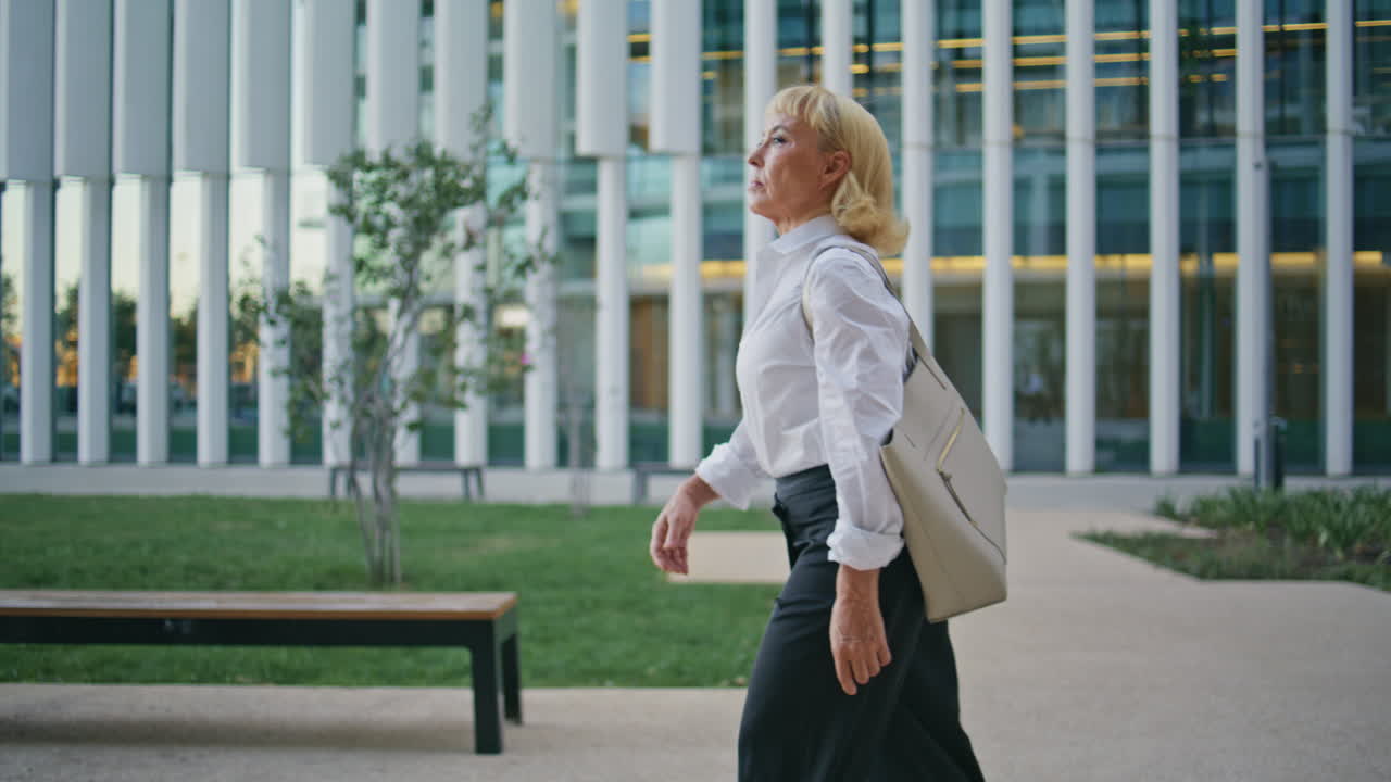 Elegant aged businesswoman walking urban street. Elderly woman going pathway