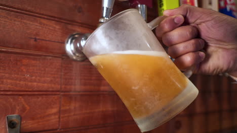 Barkeeper-Gießt-Bier-Aus-Dem-Zapfhahn,-Zieht-Hand-In-Mattierten-Becher,-Schieberegler-In-Zeitlupe----4k