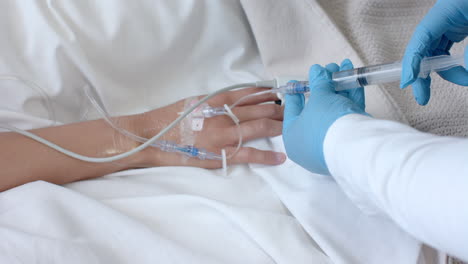 male doctor in gloves injecting drip of biracial female patient in bed with syringe, slow motion