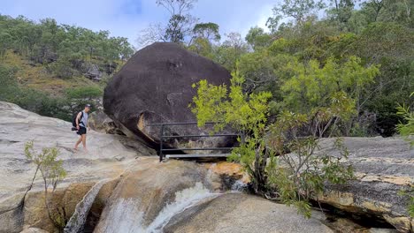 macho adulto con mochila parando en el puente al lado de boulder en emerald creek falls