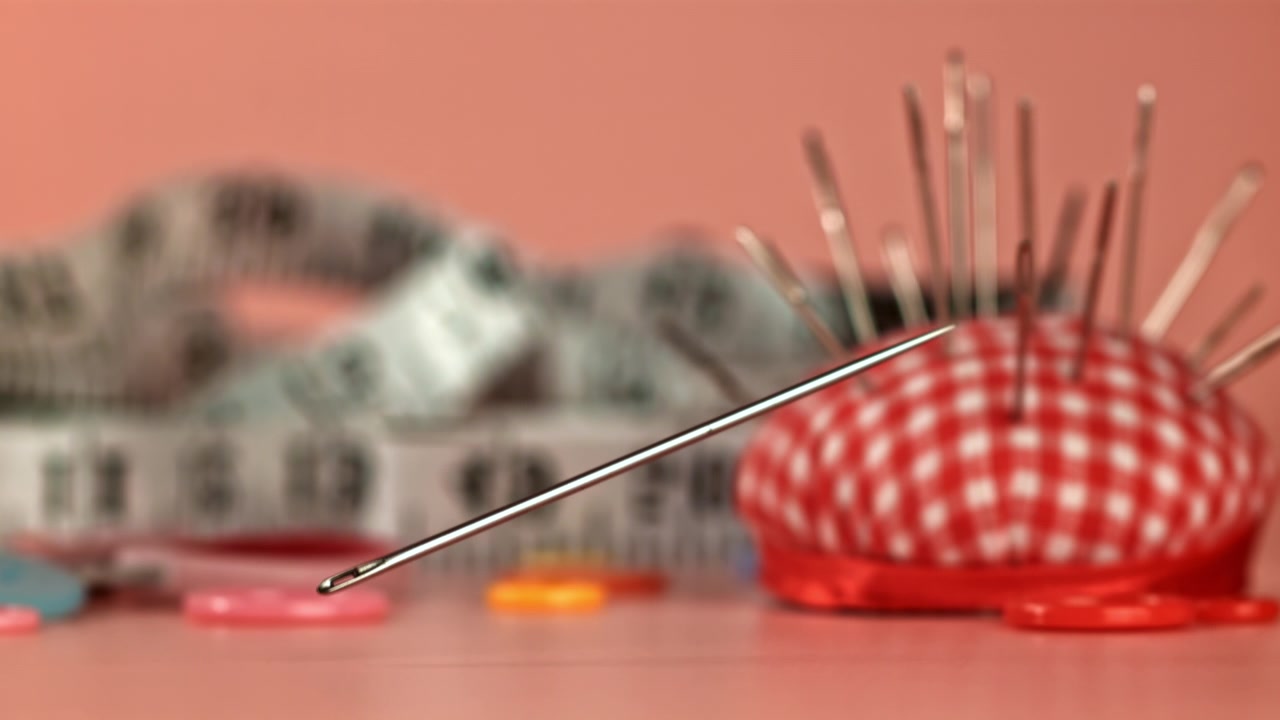 Sewing Needle Falling with Pincushion and Measuring Tape in Background