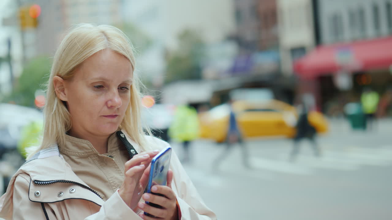 молодая женщина пользуется смартфоном на фоне офисных зданий в центре манхэттена, новый год