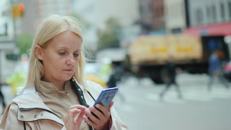 A-Young-Woman-Uses-A-Smartphone-Against-The-Backdrop-Of-Office-Buildings-In-Downtown-Manhattan-New-Y