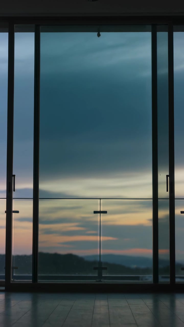 Vertical video: Filming camera showing dusk shifting through sliding doors in lounge, balcony rail