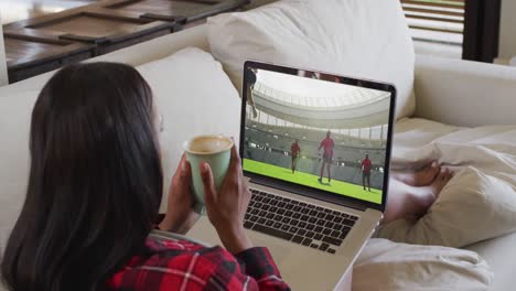 compuesto de una mujer sentada en casa sosteniendo un café viendo un partido de rugby en una computadora portátil