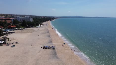 drone rises and flies quickly forward over mui ne beach, revealing white sand shore below, resorts on the left, sea on the right, and mountains on the horizon.